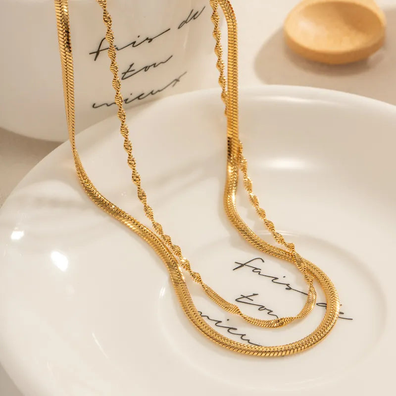 Collier Torsade double chaîne dorée présenté sur une coupelle ivoire